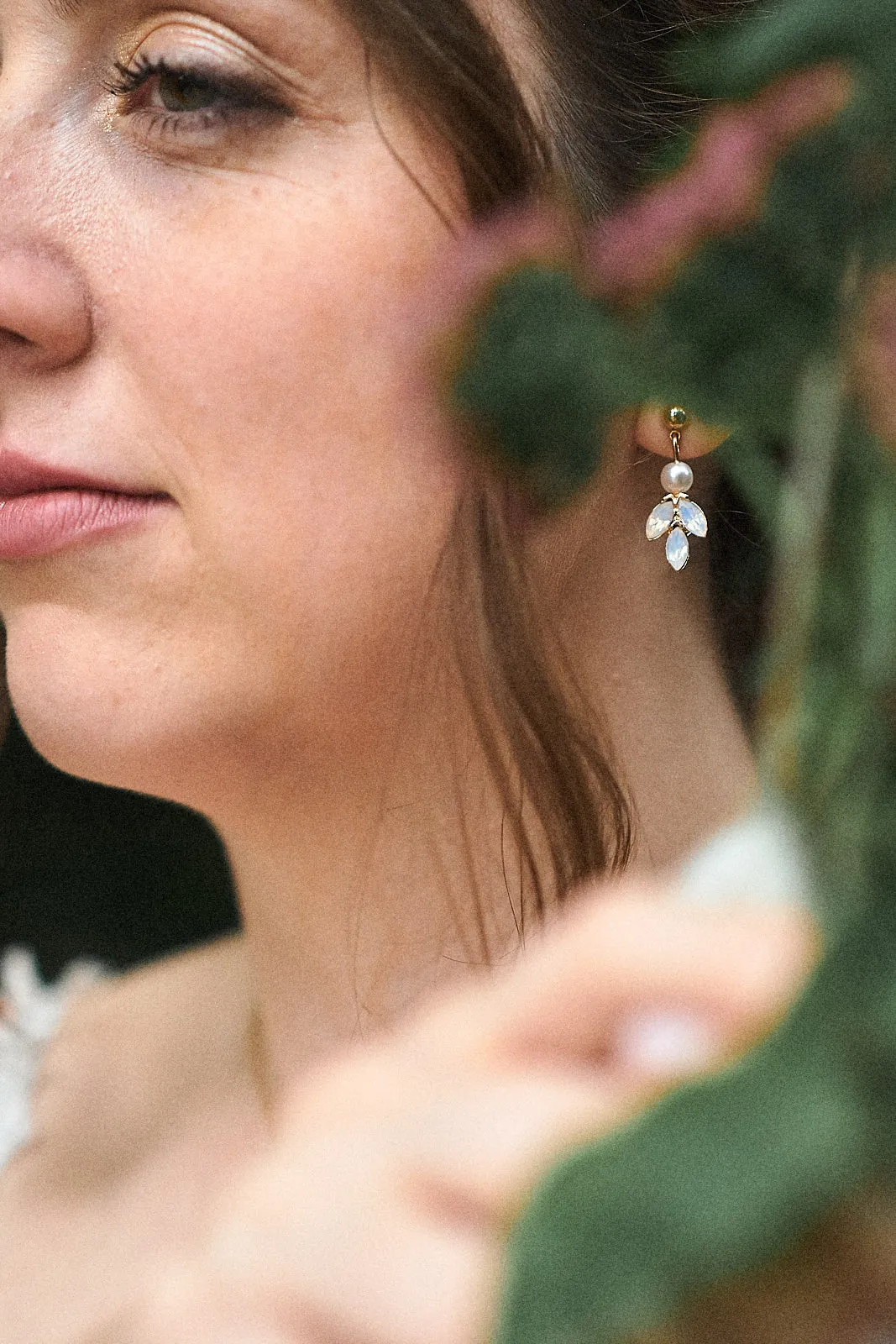 Detailaufnahme von einem seitlichen Gesicht eine Braut mit einem schönen Ohrring. im Vordergrund sind Grüne Blätter unscharf zu erkennen.
