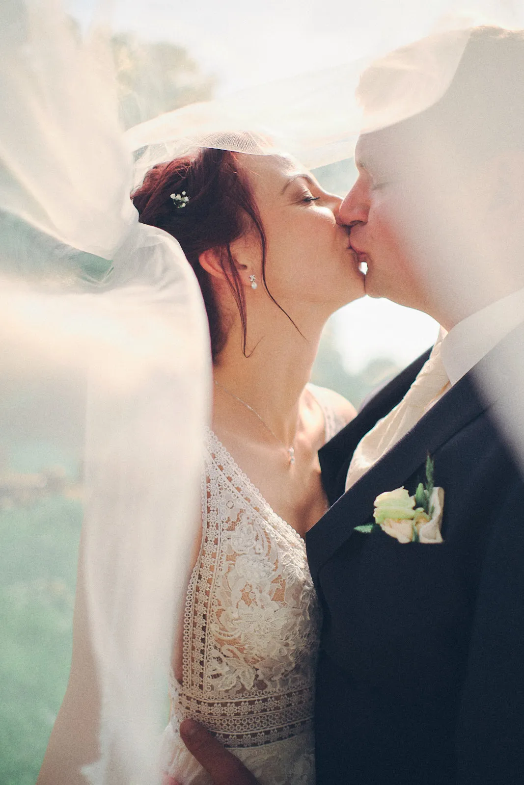 Hochzeitspaar unter einem lichtdurchfluteten Schleier küsst sich liebevoll.