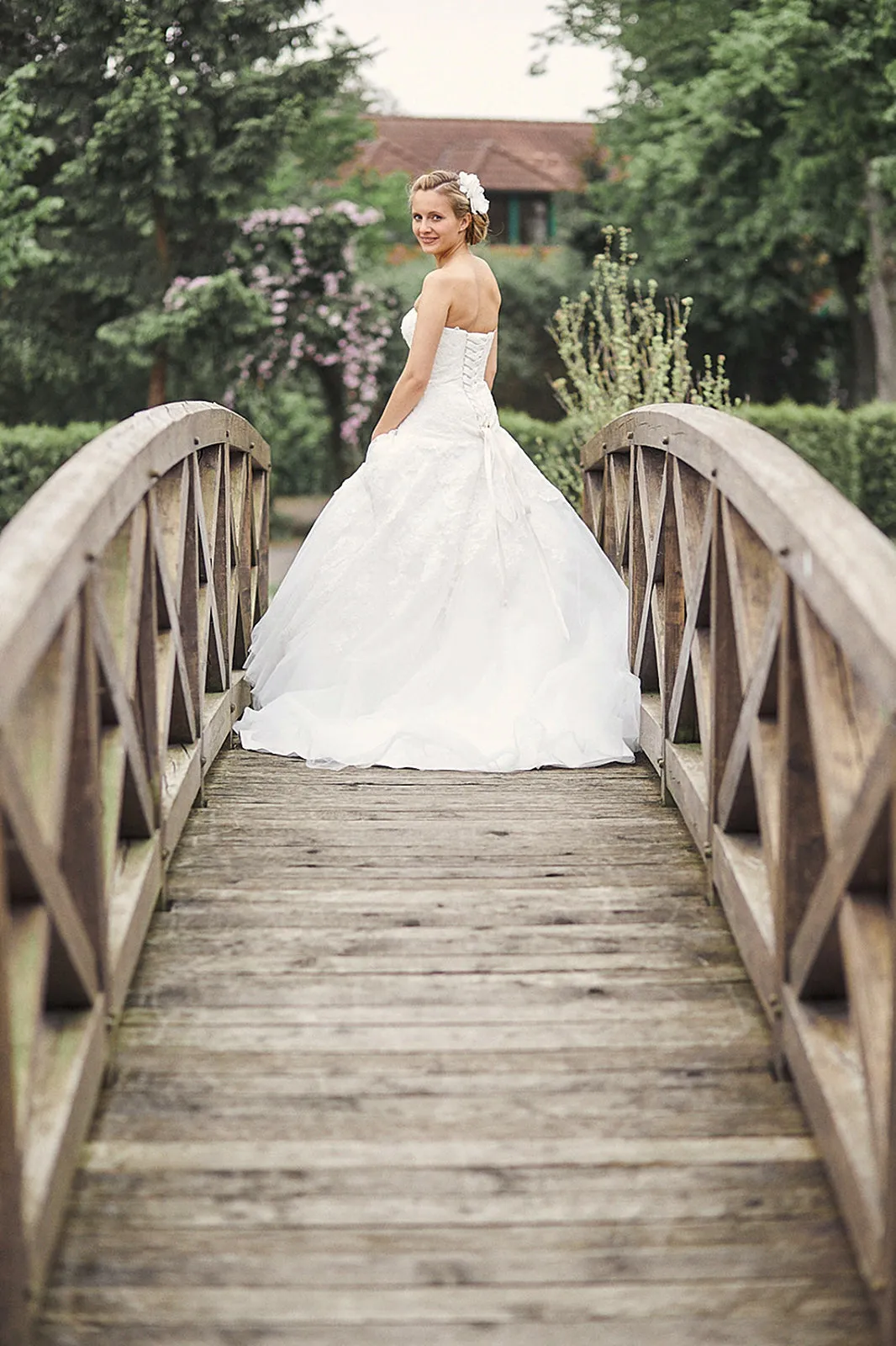 Eine Braut im weißen Kleid steht auf einer Brücke und schaut über ihre Schulter schmunzelnd in die Kamera.