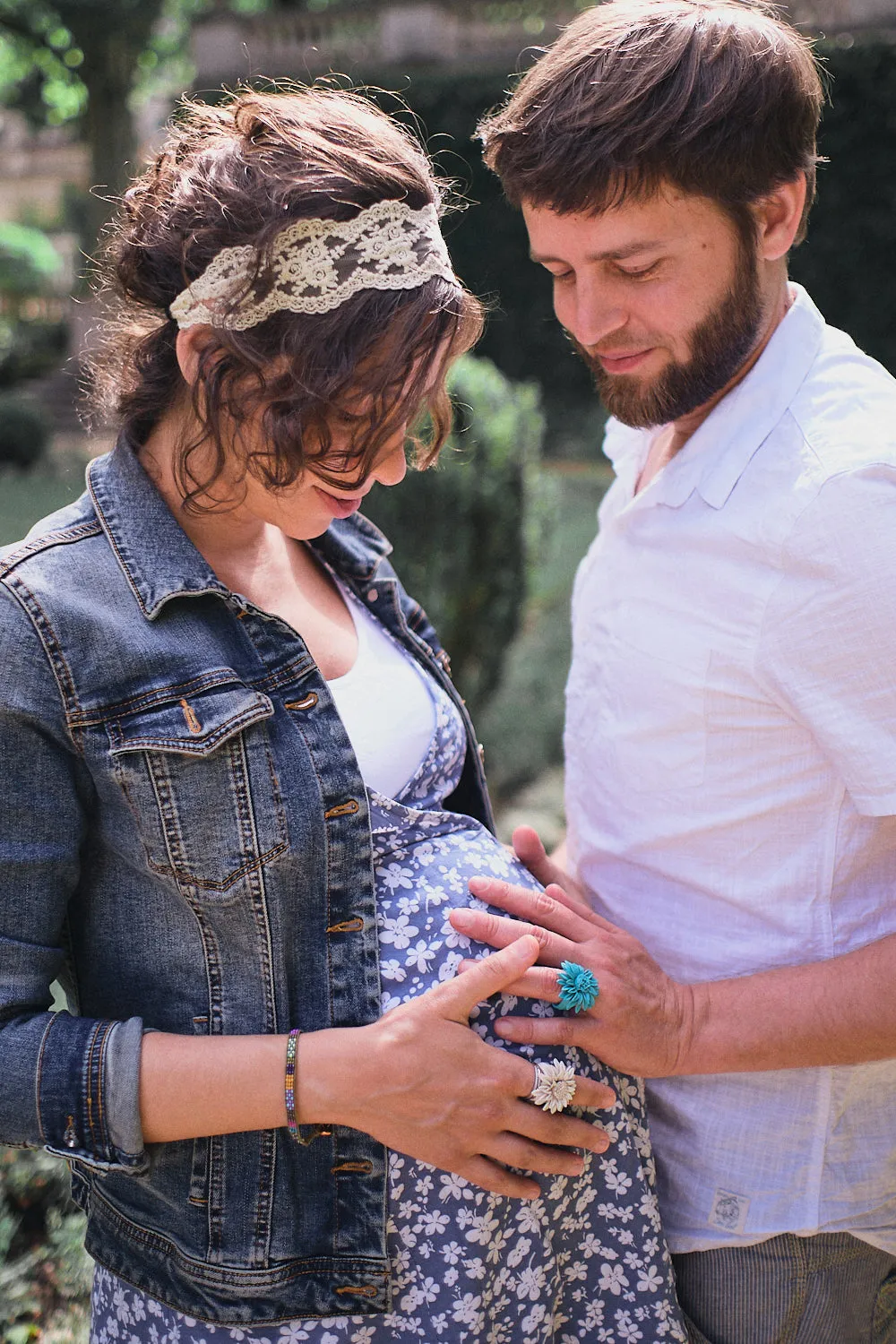 Ein junges Paar steht im Park und hält mit den Händen gemeinsam den Babybauch der Frau und fühlt ob das Kleine zu spüren ist.